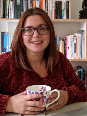 Sophie Mental Wellbeing Worker in a dark red top and holding a teacup and saucer.