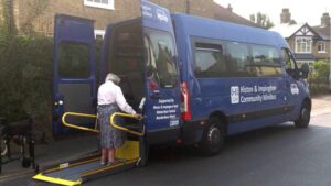 An elderly lady using the tail lift at the back of the HI Friends minibus.